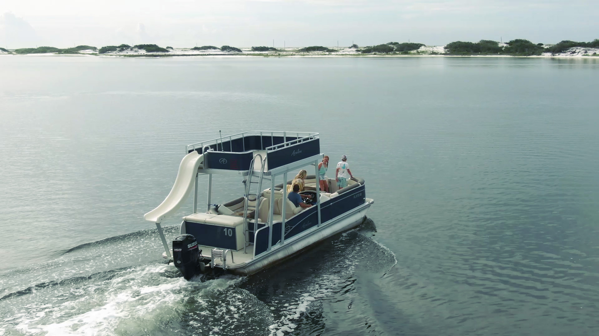 double-decker-pontoon-boat-rental-slide-navarre-florida A blue Avalon double-decker Pontoon Boat with a white Slide coming off the back idles across the glassy water of Navarre's intercoastal waterway